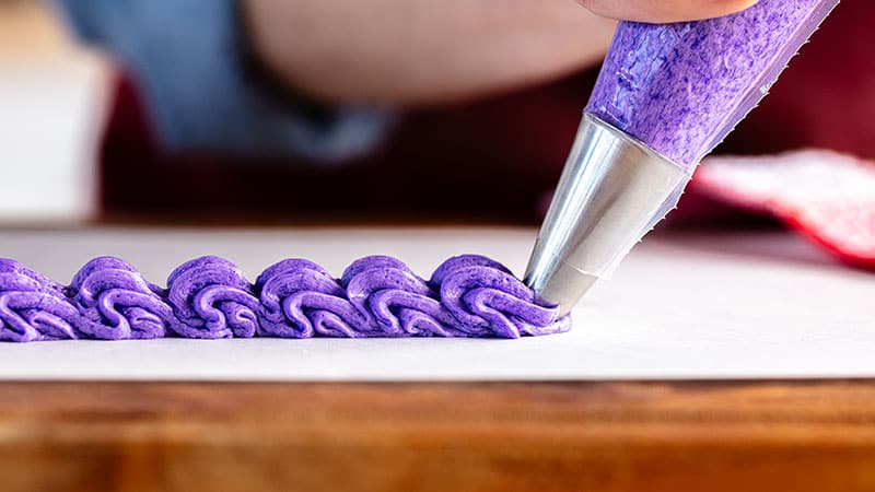 person pipes purple frosting shells onto a board