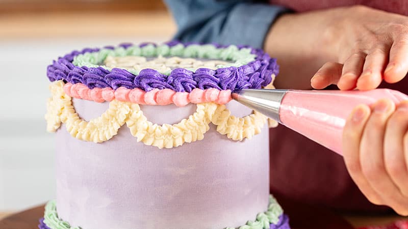 A person using a frosting bag to add intricate designs to a cake