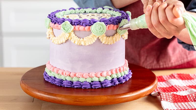 A person using a frosting bag to add green rosettes to a cake
