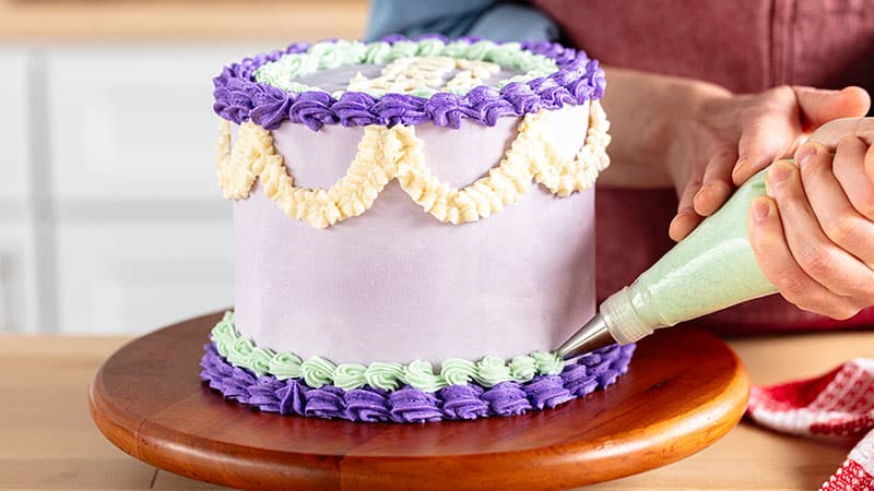 a person adding frosting decorations to a cake on a cake wheel with different shades of purple