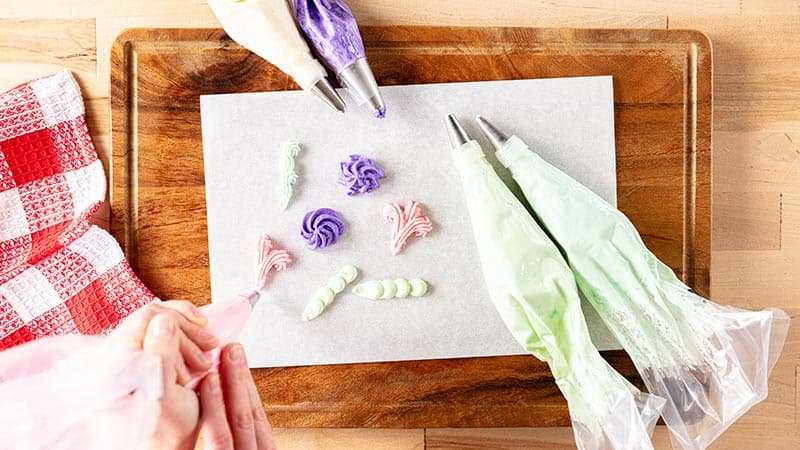 a person sampling different color frosting and piping styles with multiple bags of frosting