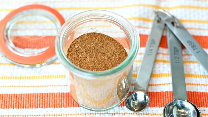 A container of spices next to three measuring spoons